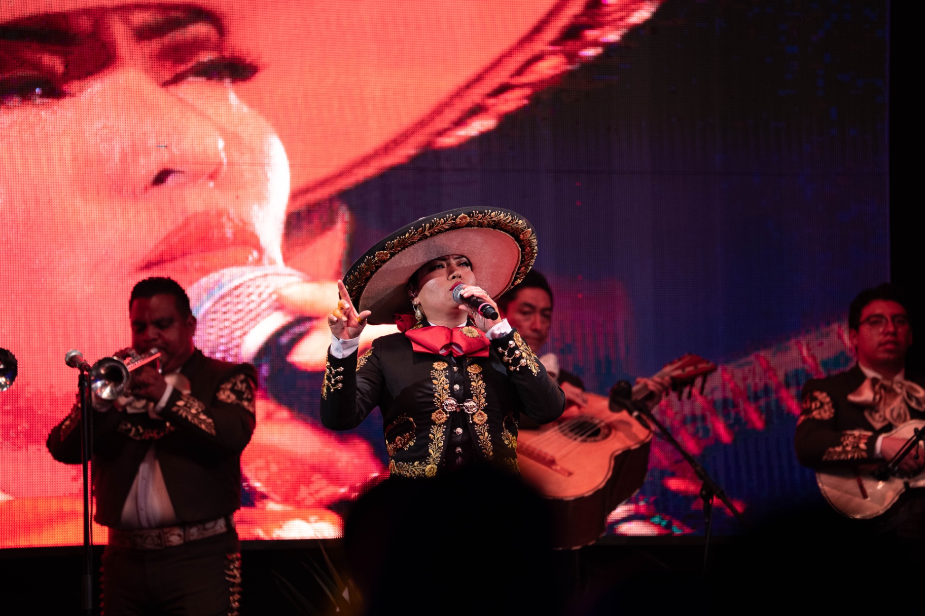 Rosario del Valle cantando con mariachi frente a una pantalla gigante